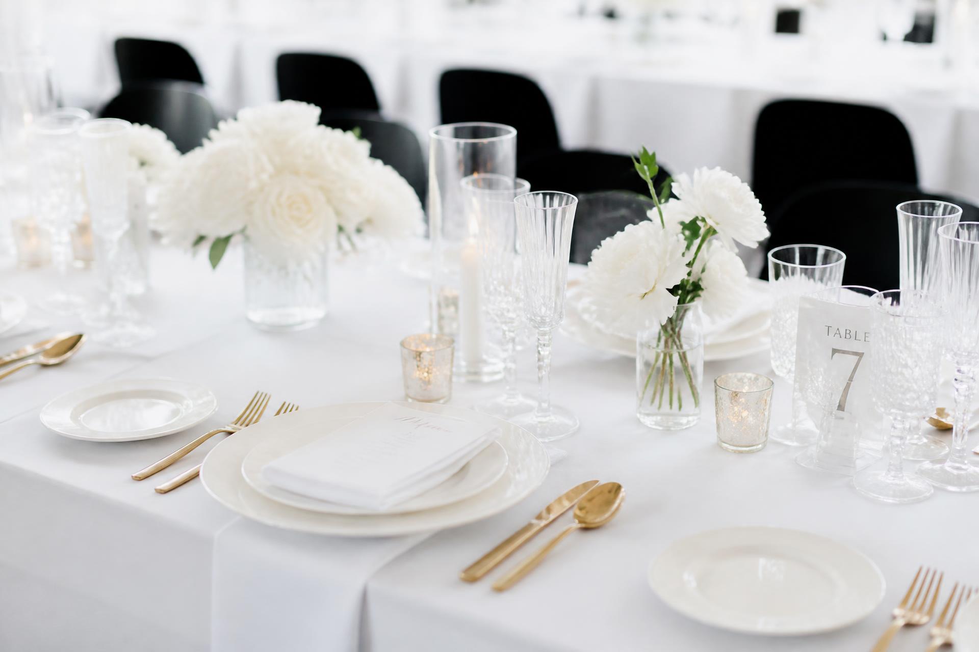 Table de mariage dressée : assiettes blanches, verrerie et couverts dorés